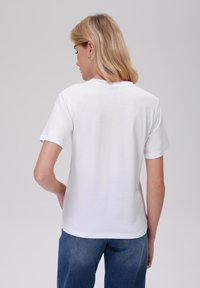 Bílý bavlněný tričko s krátkými rukávy, kulatým výstřihem, hladkou texturou a uvolněným střihem. Má jednoduchý zadní design bez ozdob.