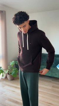 Mörkbrun hoodie med stor framficka och gräddfärgad dragsko. Kombinerad med mörkgröna mjukisbyxor, placerad i en ljus interiör.