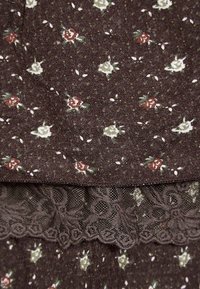 Tessuto marrone con una piccola stampa floreale in rosso, bianco e verde. La parte inferiore presenta un delicato e intricato bordo in pizzo dello stesso marrone.