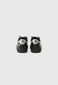 Sneaker in pelle nera con suola in gomma spessa, dettagli metallici sul tallone e design con lacci. Presenta punta arrotondata e dettagli testurizzati.