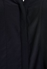 Garbìo nero con una texture liscia, dotato di cuciture verticali e una cerniera discreta. Il materiale sembra leggero e leggermente lucido.