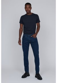 Camiseta navy, jeans ajustados azul oscuro y zapatos negros. Los jeans tienen un diseño clásico de cinco bolsillos y una textura sutil.