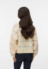 Maglione lavorato a maglia in beige con motivo traforato e dettagli in blu, arancione e viola. Vestibilità ampia con polsini e orlo a coste. Abbinato a jeans scuri.