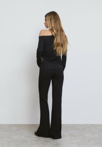Haut noir décolleté avec un détail froncé sur le côté, associé à un pantalon noir évasé. Tissu lisse et silhouette ajustée.