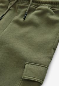 Grüne Sweatpants aus weichem Material, mit einem elastischen Bund und Kordelzügen sowie einer Seitentasche. Glatte Textur und lässiges Design.