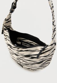Τσαντάκι ώμου από καμβά με ριγέ σχέδιο ζέβρας σε μαύρο και μπεζ, με φερμουάρ και μαύρη φόδρα που περιλαμβάνει μια μικρή εσωτερική τσέπη.