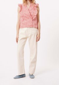 Rotes, floral gemustertes, ärmelloses Top mit rüschigen Schultern, kombiniert mit hellbeigen, geraden Hosen und weichen blauen Ballerinas.