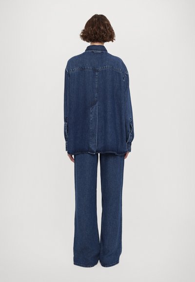 Denim outfit featuring an oversized jacket and wide-leg trousers. Both pieces are in dark blue with a soft texture and visible stitching.