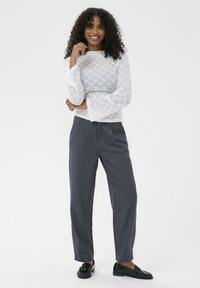 Hvid blondebluse med lange ærmer og klokkeærmer, parret med mørkegrå skræddersyede bukser og sorte loafers. Glat tekstur og tætsiddende design.