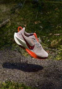 Bežecká obuv Nike vo svetlej béžovej farbe s marhuľovými akcentmi. Obsahuje štruktúrovaný zvršok, oranžový pútko na päte a vystlanú podrážku pre podporu.