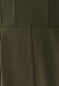 Olivově zelená látka s hladkou texturou obsahuje vertikální sklady a švové detaily, které zdůrazňují přizpůsobený design vhodný pro různé příležitosti.