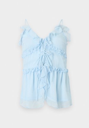 Blouse sans manches bleu clair avec détails à volants, fermeture nouée à l'avant et fines bretelles sur fond blanc.