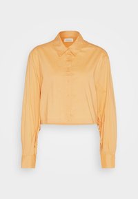 Chemisette orange vif, dotée d'un col classique, d'une fermeture à boutons sur le devant, de manches longues avec des poignets à boutons, et d'un tissu léger et lisse.