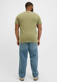 Olivgrünes T-Shirt mit kurzen Ärmeln, Rundhalsausschnitt und taillierter Passform, kombiniert mit hellblauen, locker sitzenden Jeans.