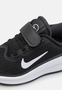 Zwarte sportschoen met een bovenwerk van mesh, witte Nike swoosh, verstelbare band en een gevoerde zool met een gestructureerde, antislip onderkant.