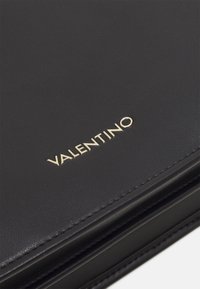 Svart läderplånbok med en slät yta, guld "VALENTINO"-logotyp och exakt sömnad längs kanterna. Kompakt design med minimal hårdvara.