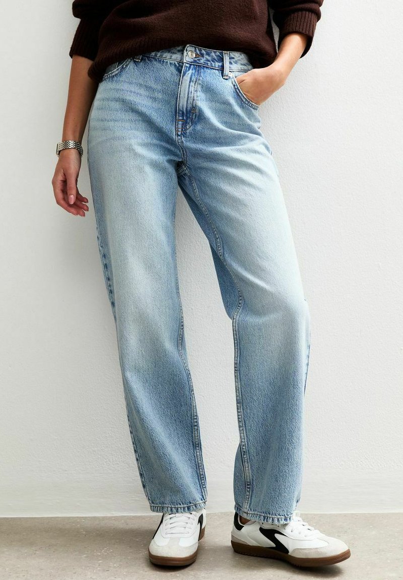 Jeans de mezclilla azul claro con cintura alta, diseño de pierna recta y un ligero desteñido. Combinados con zapatillas blancas con acentos en negro.