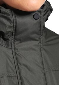 Tmavě zelená voděodolná bunda s vysokým límcem, zapínáním na zip a černým knoflíkem s logem "Hunter" na krku. Hladká, lesklá textura.