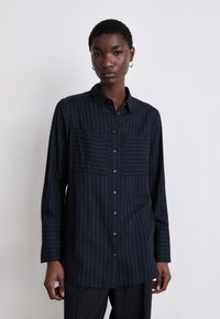 Dark navy button-up shirt featuring vertical white pinstripes, two chest pockets, and long sleeves. Made of smooth fabric with a collar.