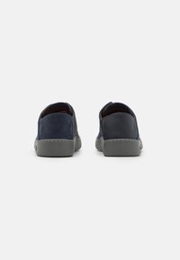 Scarpe in camoscio e pelle blu navy con suola in gomma grigia, caratterizzate da dettagli cuciti e una punta arrotondata. Vista posteriore che mostra il taglio basso.