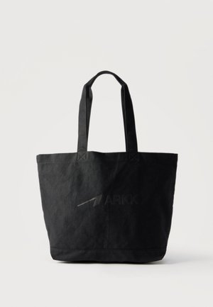 Μαύρη υφασμάτινη τσάντα ώμου με διπλές λαβές και διακριτικό ανάγλυφο λογότυπο "ARKK" στο μπροστινό μέρος, ακουμπισμένη σε απλό λευκό φόντο.