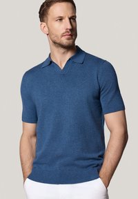 Koszulka polo z krótkim rękawem w głębokim niebieskim kolorze z dzianiny. Posiada dekolt w kształcie litery V, prążkowane mankiety i dół, a także dopasowany i gładki materiał.