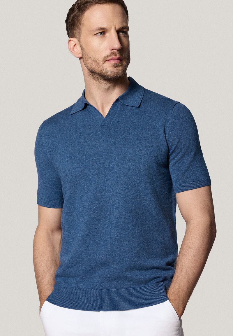 Koszulka polo z krótkim rękawem w głębokim niebieskim kolorze z dzianiny. Posiada dekolt w kształcie litery V, prążkowane mankiety i dół, a także dopasowany i gładki materiał.