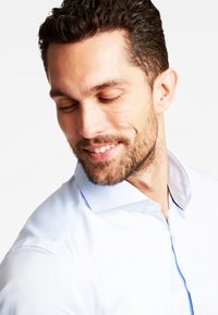 Camicia azzurro chiaro con colletto alla francese, caratterizzata da una texture liscia e una leggera lucentezza, arricchita da contrasti nei dettagli del colletto.