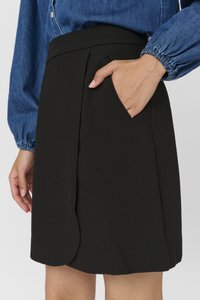 Jupe noire en tissu texturé, avec une taille cintrée, une poche frontale en biais et un ourlet arrondi, assortie à une chemise en denim.