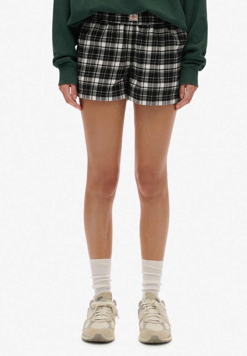 Zwart-witte geruite korte broek met elastische tailleband en twee zijzakken, gemaakt van een lichtgewicht stof, gecombineerd met beige sneakers.