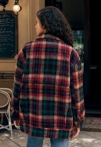 Ruudline villane tehnika punastes, rohelistes ja kollastes toonides, suurte kraede, nööbitavate mansettide ja avara lõikega. Mustriline tekstuur on silmatorkav.