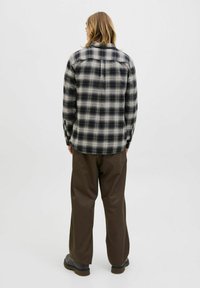Camisa de franela a cuadros en blanco y negro, con cuello y puños abotonados, combinada con pantalones sueltos marrones y zapatos negros.
