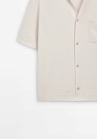 Lichtbeige kortarmpoloshirt van zacht materiaal. Heeft een kraag, knoopsluiting aan de voorkant, een enkele borstzak en een effen textuur.