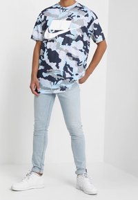 Kamouflage t-shirt i blått, grått och vitt med en stor vit Nike-logotyp. Kombinationen med ljusblå skinny jeans och vita sneakers.
