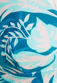 Roupa de banho com um design tropical apresentando grandes folhas em tons de aqua e azul claro sobre um tecido texturizado, realçado por detalhes em branco e azul escuro.