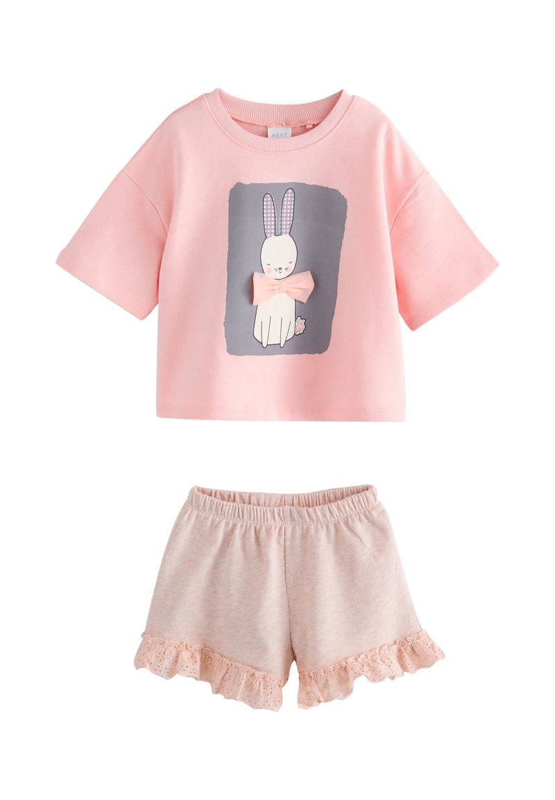 T-shirt à manches courtes rose clair avec un motif de lapin et un nœud, assorti à un short rose clair avec un ourlet en dentelle à volants. Matière en coton doux.