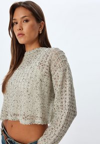 Maglione grigio corto con un design a maglia open-knit testurizzato, caratterizzato da un colletto aonde e maniche lunghe, abbinato a pantaloni in denim.