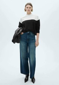 Black and white color-blocked sweater, paired with high-waisted wide-leg blue jeans and black pointed toe boots; sleek, modern design.