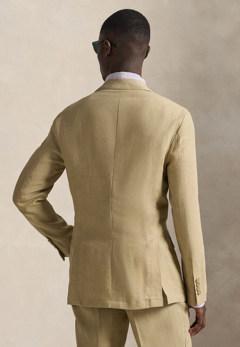 Beige linen suit jacket with a tailored fit, single vent at back, and three buttons on cuffs. Smooth texture and structured design.