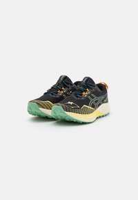 Zapatillas de correr en negro y amarillo con un upper de malla texturizada. Presentan acentos en naranja y una suela de goma verde con patrones de tracción.