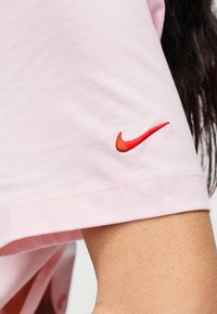 Ανοιχτό ροζ βαμβακερό t-shirt με κόκκινο κεντημένο λογότυπο Nike στο μανίκι, με καθαρές ραφές κ αι χαλαρή εφαρμογή.