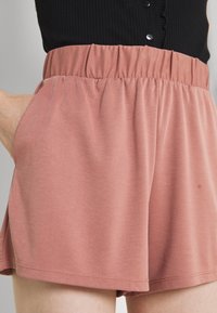Ružové šortky s elastickým pasem vyrobené z měkké tkaniny, s bočními kapsami, uvolněným střihem a lemem těsně nad stehnem.