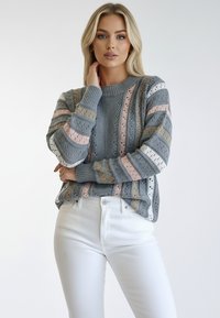 Szary sweter dzianinowy w poziome paski w kolorach różowym, miękkim żółtym i białym. Ma prążkowany dekolt i wzorzyste rękawy. W zestawie z białymi spodniami.