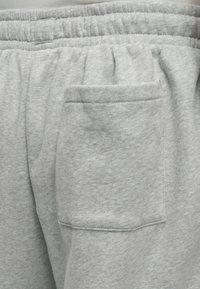 Pantalon de survêtement gris clair avec une taille élastique et une poche plaquée rectangulaire cousue à l'arrière, côté droit.