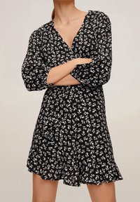 Černé šaty s květinovým potiskem v bílé barvě. Mají výstřih do V, dlouhé rukávy a rozšířený lem se sklady.