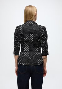 Zwarte blouse met witte polkadots, driekwart mouwen, een getailleerde taille en een peplumzoom. Glad stof met witte stippen, maatwerk ontwerp.