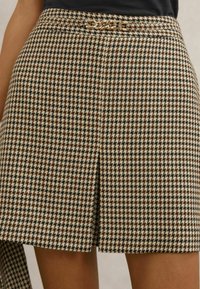 Rudos ir kreminės spalvos languoti šortai tiesiu kirpimu, su grandinėlės akcentu liemens juostoje ir tekstūruota austine medžiaga.