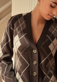 Brown and cream argyle patterned cardigan with a v-neck, featuring four circular buttons and soft knit texture.