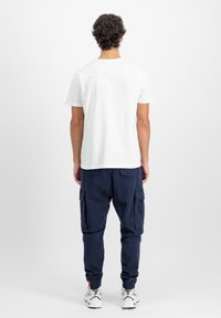 Tricou alb din bumbac, cu mânecă scurtă; pantaloni cargo bleumarin cu buzunare laterale, manșete dantelate; adidași albi cu accente negre.