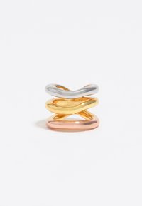 Tres anillos entrelazados en plata, oro y oro rosa. Formas suaves y redondeadas con un acabado reflectante y anchos variables.